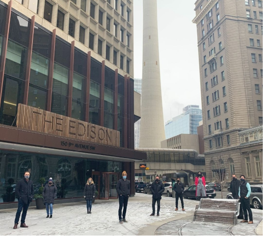 The photo shows the Edison, which is an office building in downtown Calgary, 360's first physical office location. The photo has 9 of 360's original employees posing in front of the entrance to the building.